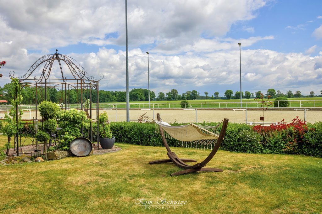 Gartenbereich des Reiterhofs Conrad mit Hängematte, Wiese und Reitplatz im Hintergrund.